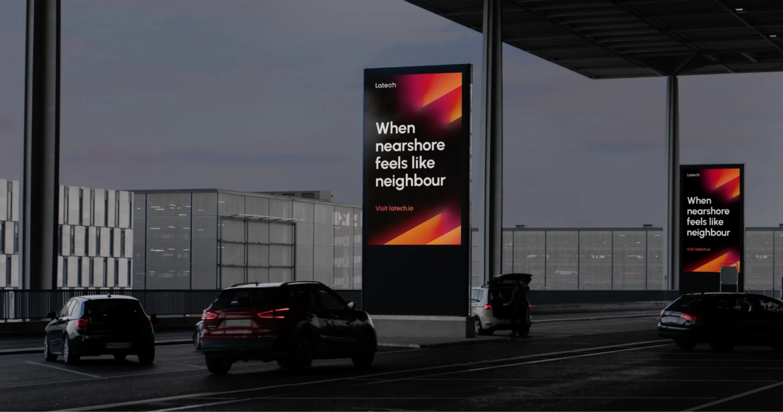 Mockup of an airport parking lot, with a vertical advertising screens displaying an ADV for Latech, reading When nearshore feels like neighbour. Part of the Latech (Stravos) project, a Tech startup rebrand by Fabio Besti Interdisciplinary Design for Nemesis Agency